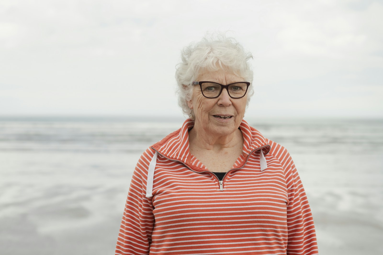 Mujer mayor sonríe con serenidad frente al mar durante un viaje.